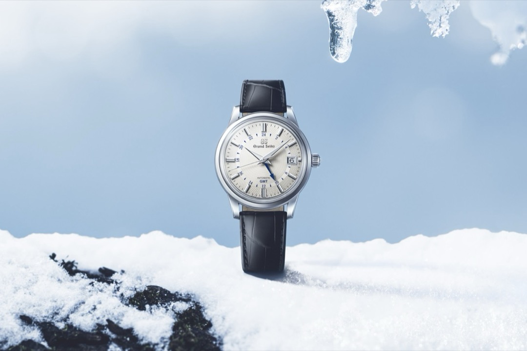 A Grand Seiko SBGM255 standing in snow, its cream guilloche dial radiating from the centre and carrying a blue 24 hour scale, a blue arrow tipped hand and a date window at three