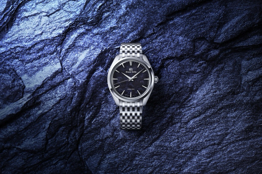 A Grand Seiko SBGY043 resting on blue grey rock, its deep indigo dial mottled with a cloud like pattern, in a slim polished case on a steel bracelet