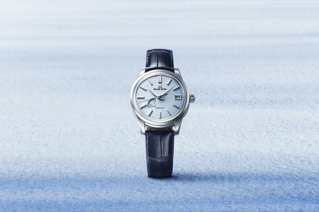 A Grand Seiko SBGA407 standing in snow, its light ice blue dial covered in a wind swept ripple texture, with a power reserve arc near eight and a date window at three