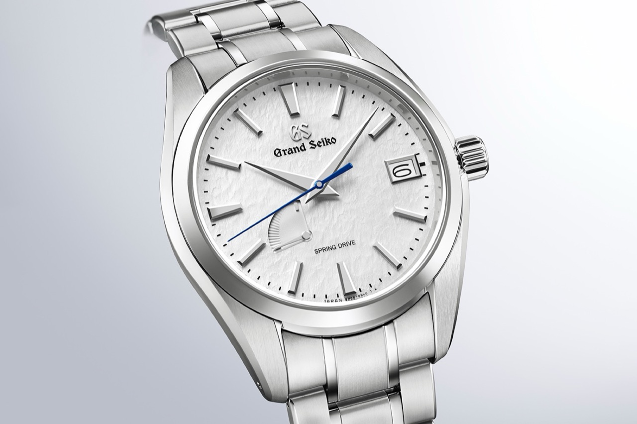 A Grand Seiko SBGA211 at a three-quarter angle, its white Snowflake dial carved into an irregular rippled relief, with faceted applied indices, a power reserve arc near eight and a blued seconds hand