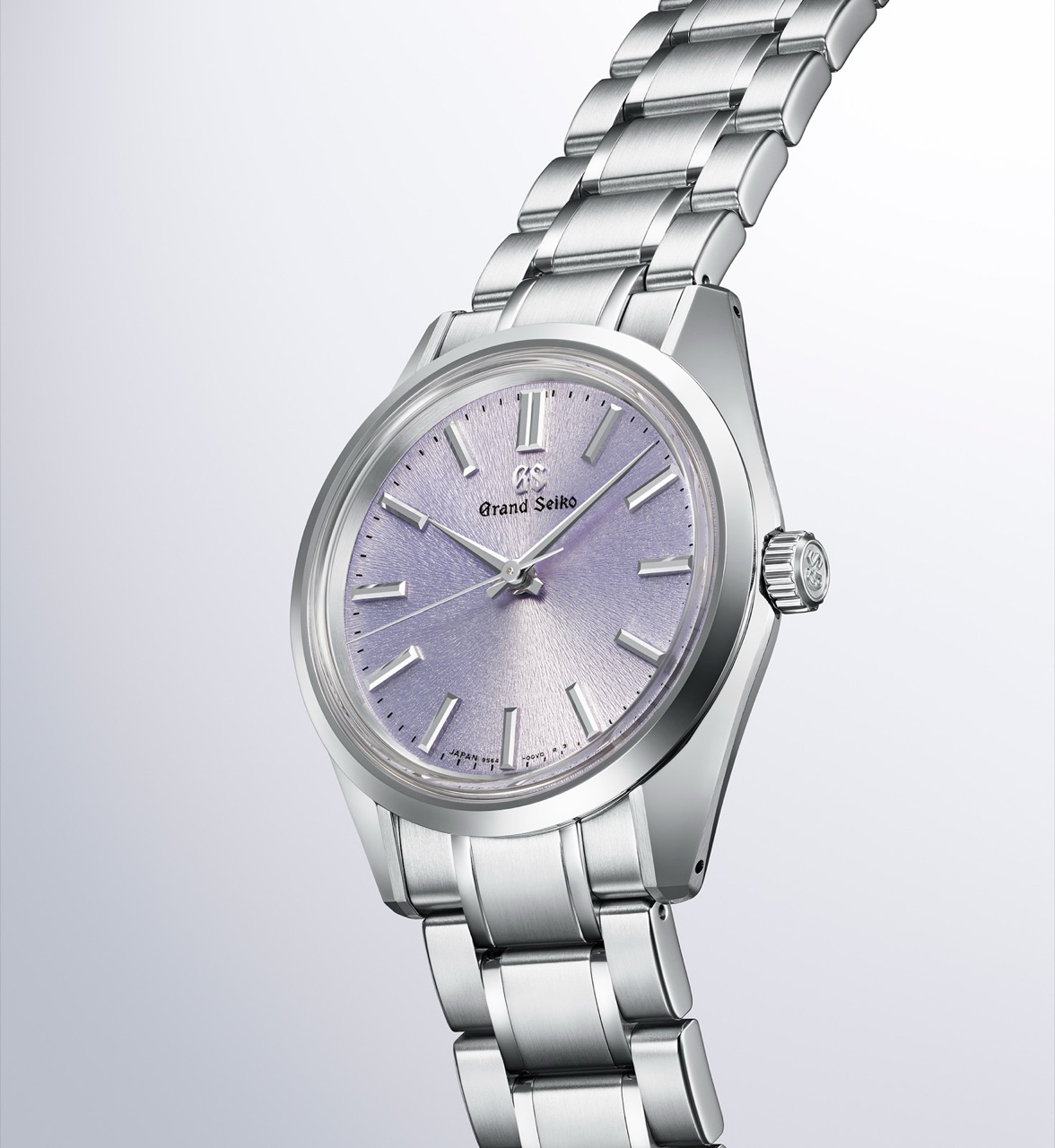 A Grand Seiko SBGW323 on a steel bracelet at a three-quarter angle, its pale lilac dial beside mirror-polished case flanks that meet hairline-brushed lug tops along a sharp ridge