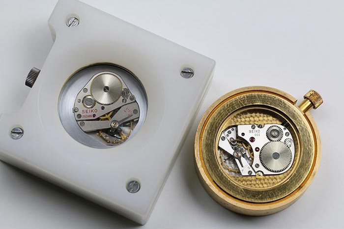 Two Seiko competition movements photographed from above, the left one held bare in a white carrier plate with its bridge stamped SEIKO in red, the right one fitted into a gold case with a crown
